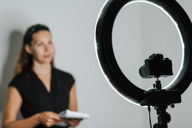 A woman records a video in front of a camera and ring light.
