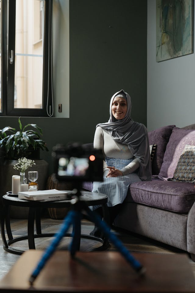 A camera on a tripod records a woman as she speaks.
