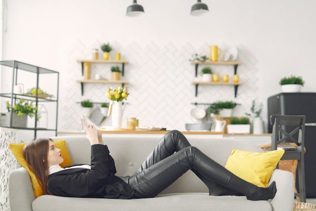 A man lies on a couch while holding up her phone.
