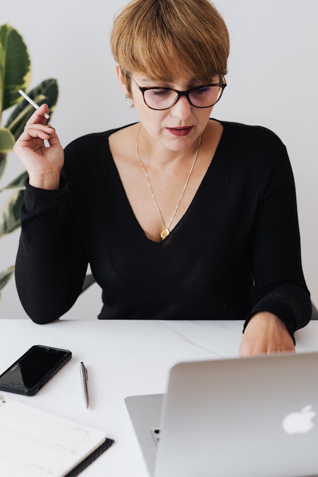 A woman types on her laptop with her phone next to her.