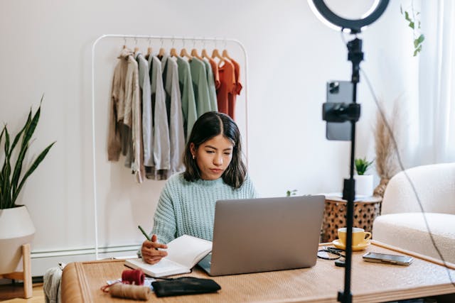 A woman writes notes as she looks at her laptop.
