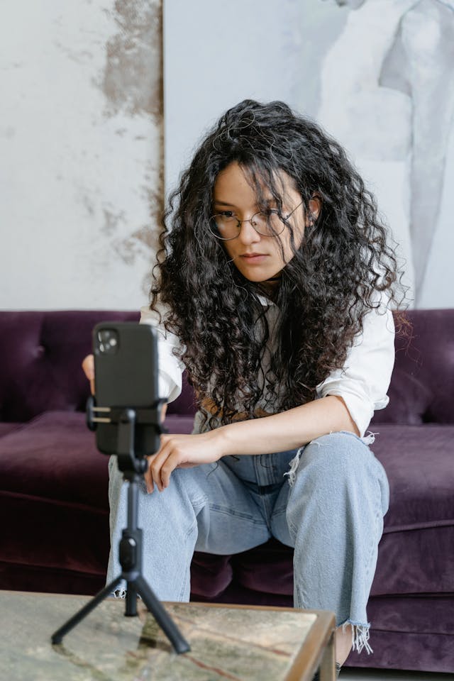 A woman with big curly hair sets up her phone on a tripod.
