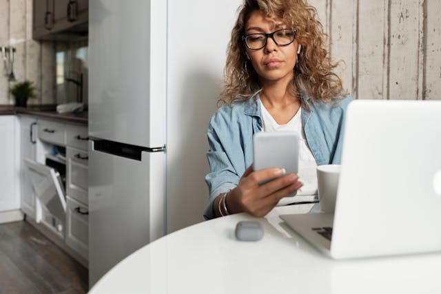 A woman in glasses looks at her phone.
