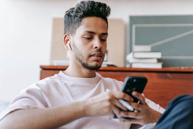 A man with AirPods and a pen types on his smartphone.