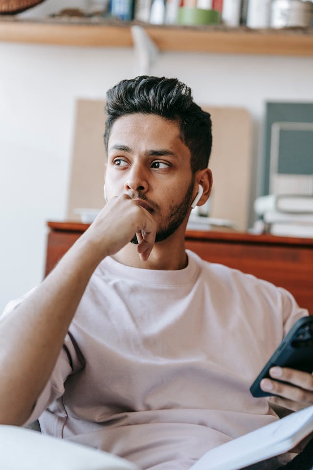 A man holding a phone looks into the distance pensively.
