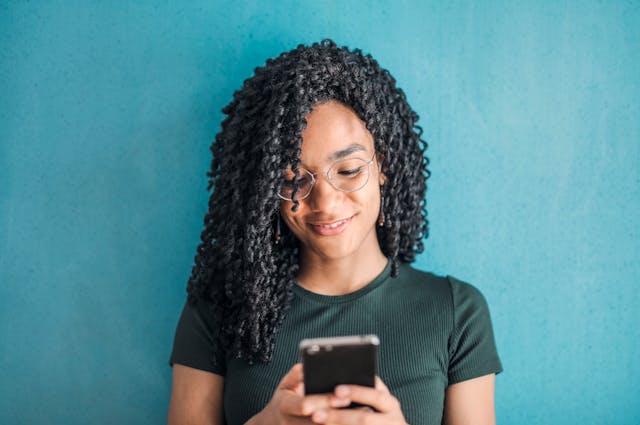 A black woman types on her cell phone.
