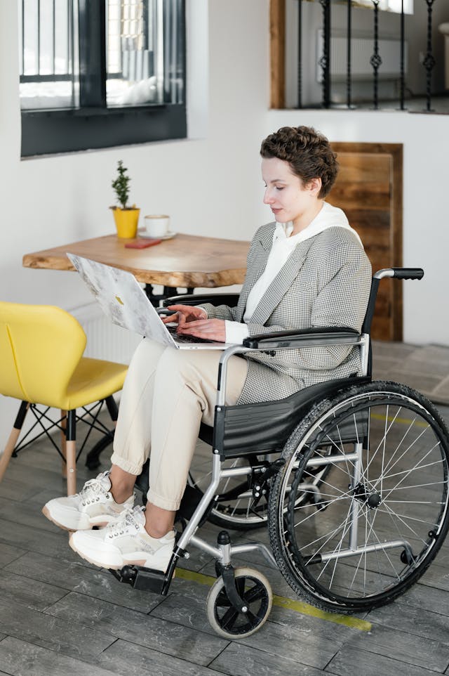 A woman in a wheelchair types on her laptop.
