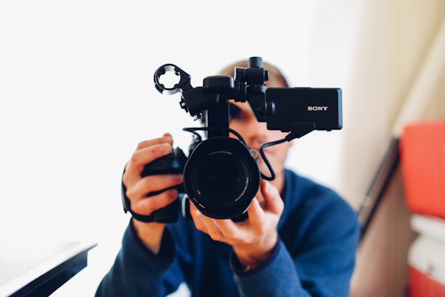 A filmmaker holds a black DSLR camera to shoot a video. 