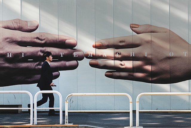 A person walks in front of a big ad on a wall which shows two hands touching each other’s fingertips. 

