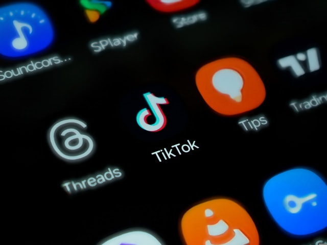 A phone’s home screen shows the TikTok app logo alongside other app logos. 
