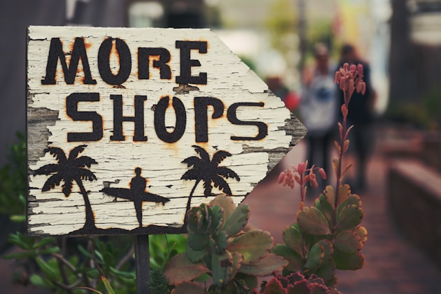 A white wooden sign says, “More Shops.”
