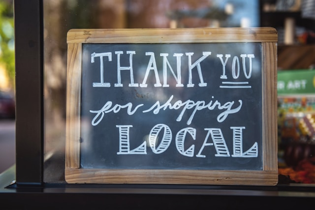 A chalkboard sign in a store window says, “Thank you for shopping local.”
