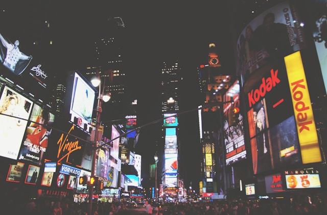 Big, digital billboards on the sides of buildings light up a busy street at night. 
