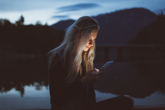 A woman sits by a lake and watches TikTok videos on her phone. 
