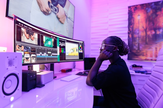 A person sits in front of two big monitors and edits content using professional video editing tools.