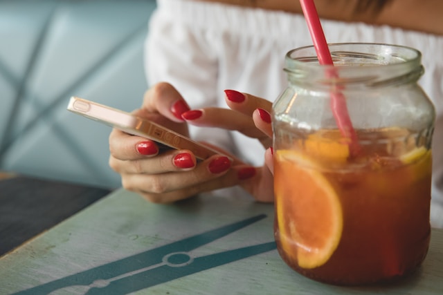 A woman edits a TikTok video on her phone while enjoying a jar of fresh orange juice.
