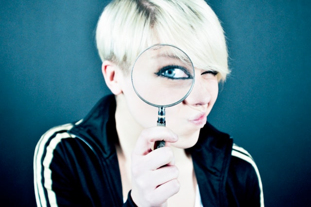 A woman in a black jacket holds a magnifying glass over one eye. 
