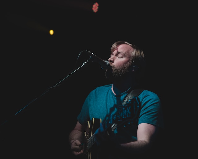 A performer stands in front of a microphone and plays the guitar while he sings. 
