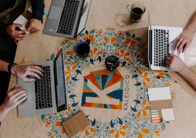 Three people sit around a table and work using their laptops.