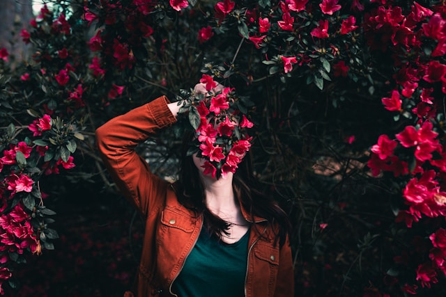 Uma mulher esconde seu rosto atrás de um ramo de flores vermelhas.