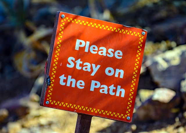 A sign on a hiking trail says, “Please stay on the path.”
