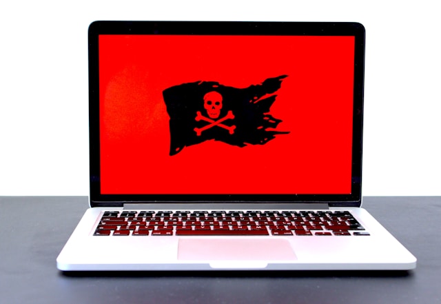 A laptop screen shows up red with a skull and two bones on a tattered black flag. 
