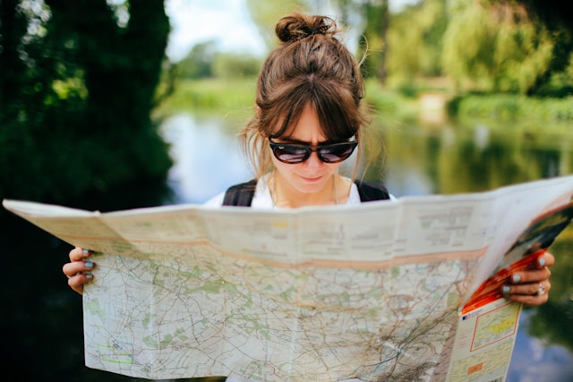 A woman in a park studies a map. 
