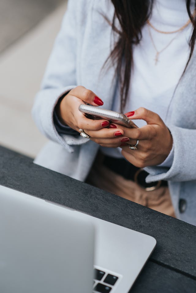 A person with red nails uses a cell phone.
