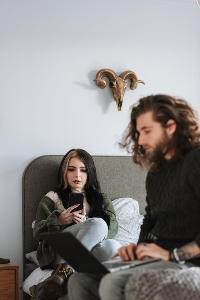 A woman uses a phone while a man uses his laptop.