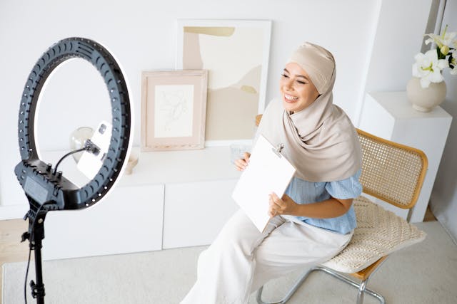 A woman records herself speaking to her phone and a ring light.
