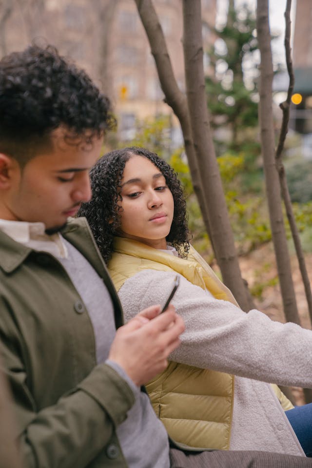 A woman sneaks a glance at a man’s phone. 
