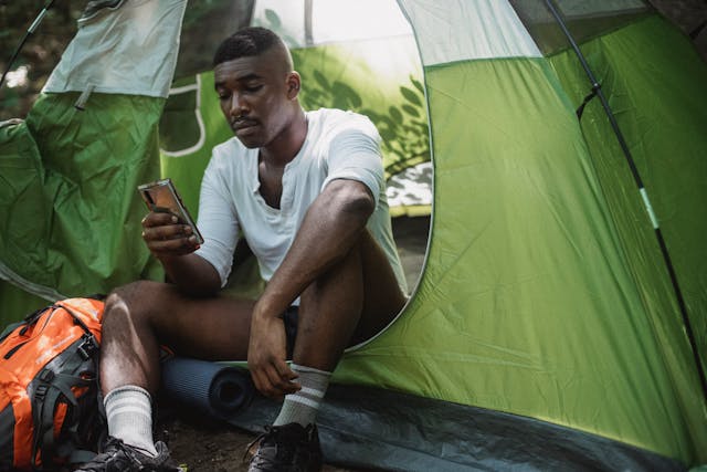 A man sitting in a tent uses his phone.
