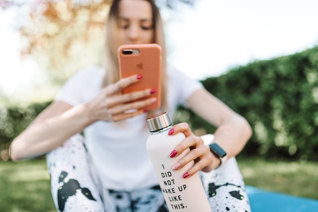 A woman in workout clothes uses her phone while she sits on the ground.
