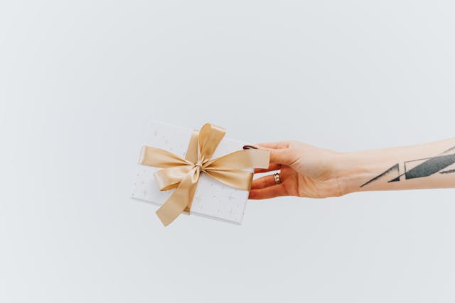 A person with a tattooed arm shares a wrapped gift box.
