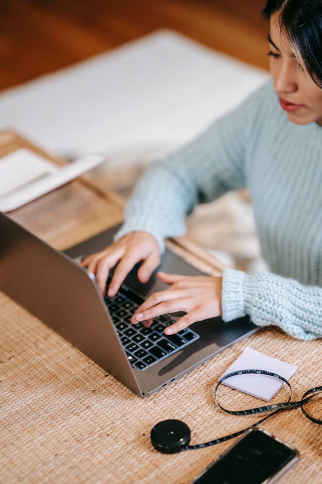 A woman in a blue knit sweater types on her laptop.
