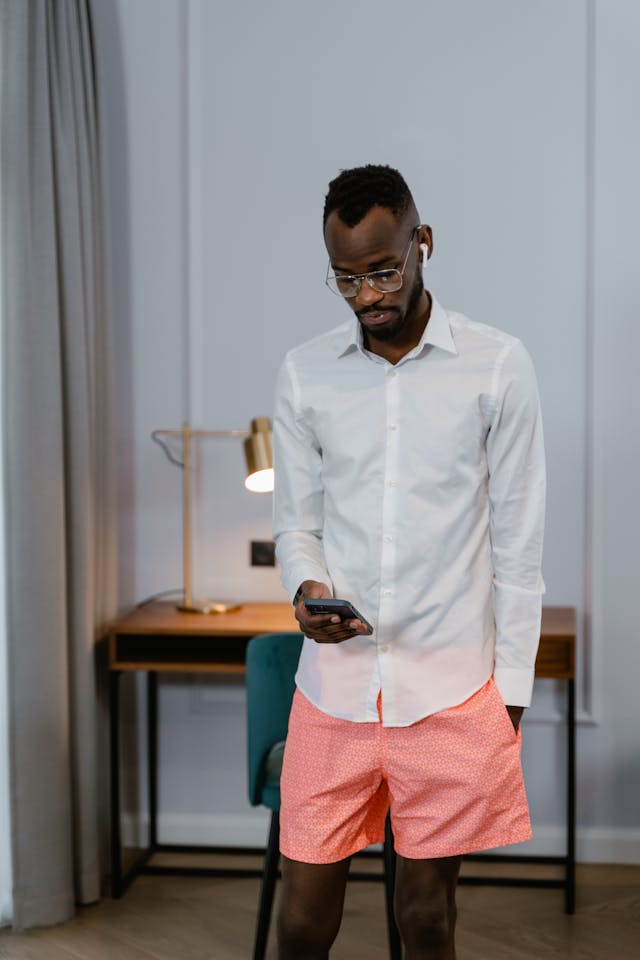 A tall man with glasses scrolls on his cell phone.
