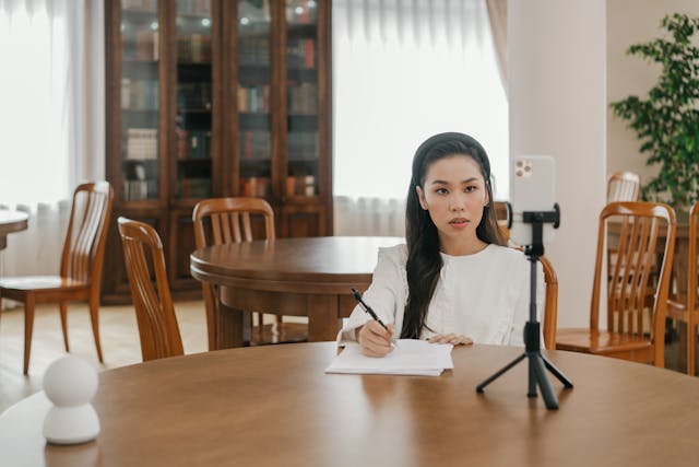 A woman makes notes as she stares at her mounted phone screen.
