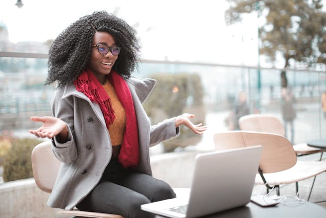 A woman in a coat happily uses her laptop.
