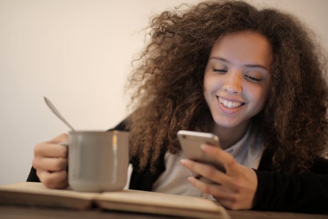 A young lady grins while she looks at her phone.
