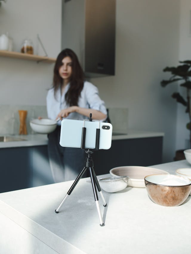 A woman looks at her phone’s camera as she mixes a dish.
