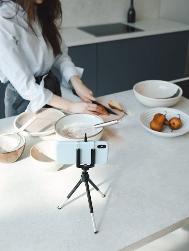 A phone on a tripod records a woman cooking.
