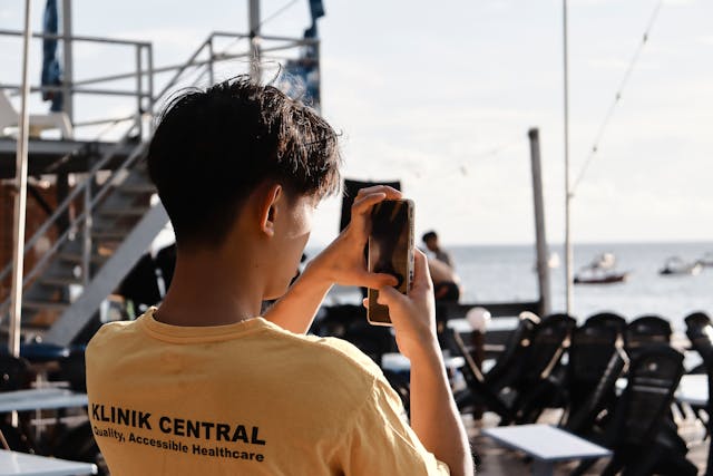 A man takes a photo of the water in the distance.
