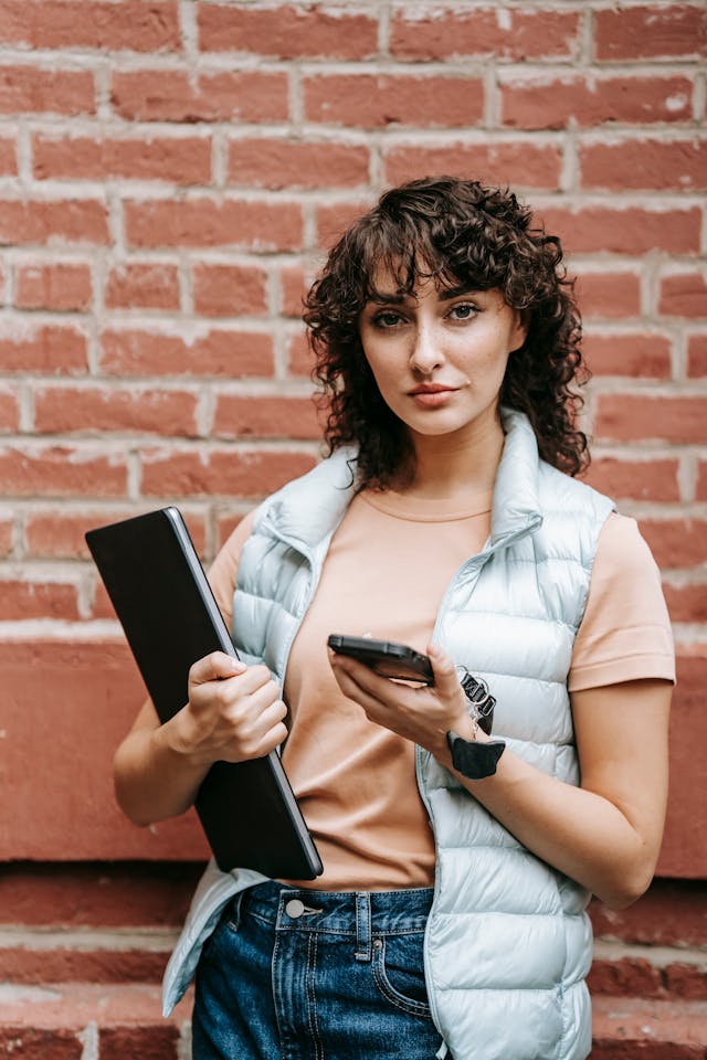 A woman holds her phone and laptop.