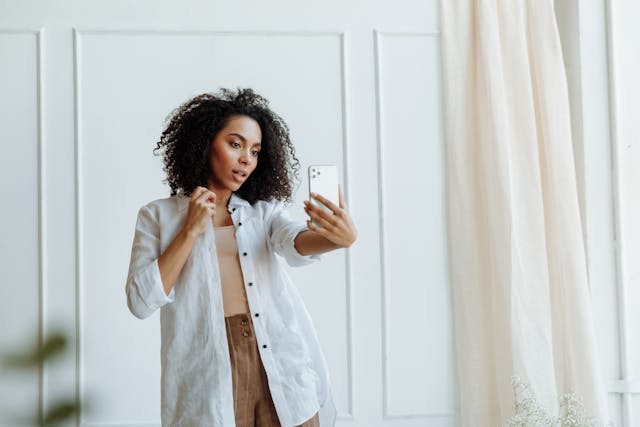 A woman with an afro takes a photo of herself.
