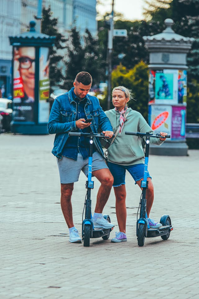 A couple stops riding scooters to look at a phone.
