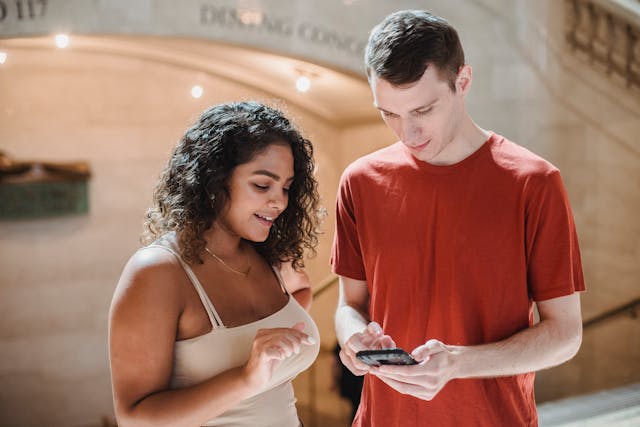 A woman looks at the phone a man is holding.
