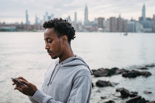 A man in a gray sweater taps on his phone.
