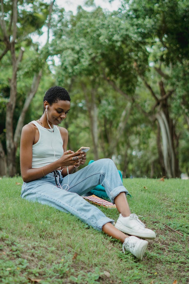 A woman sits on the grass as she uses her phone.
