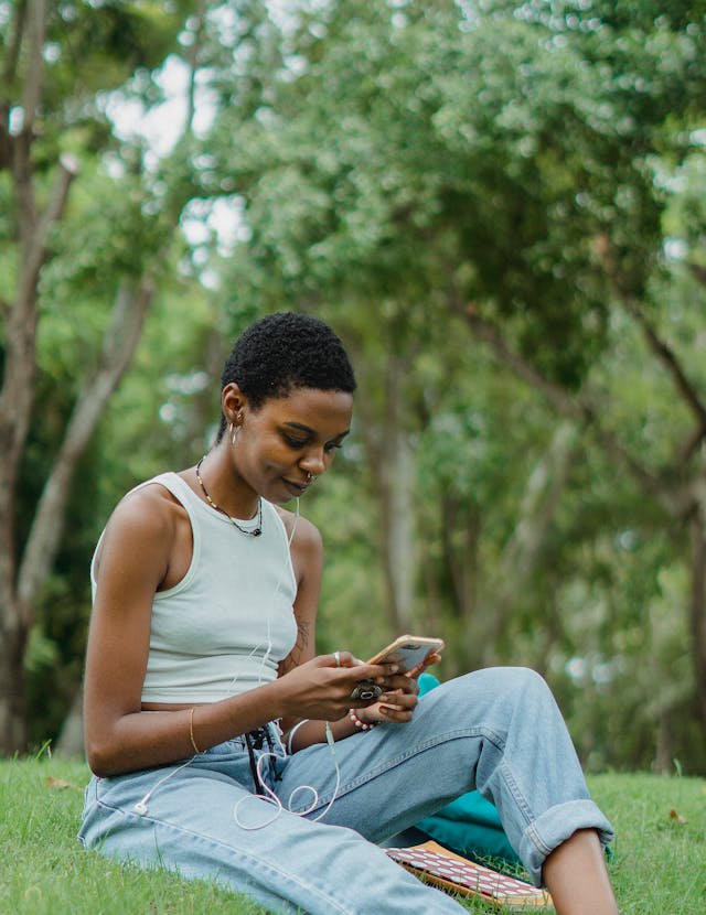 A woman sits on grass as she looks at her phone.
