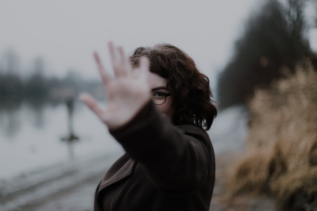 A woman wearing glasses blocks half of her face with her hand. 
